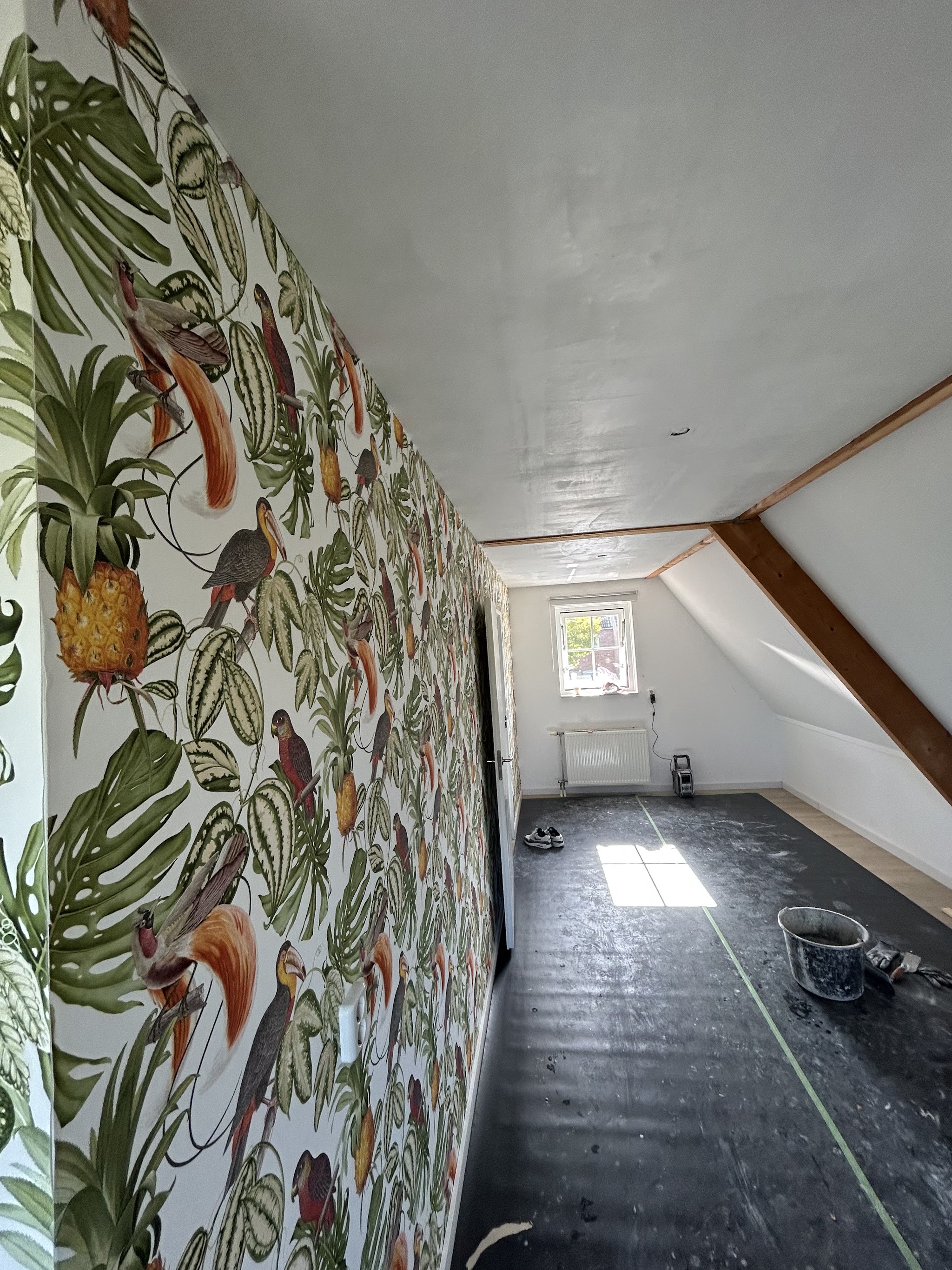 Zolderkamer met gestuct plafond en een behangen muur met tropische print