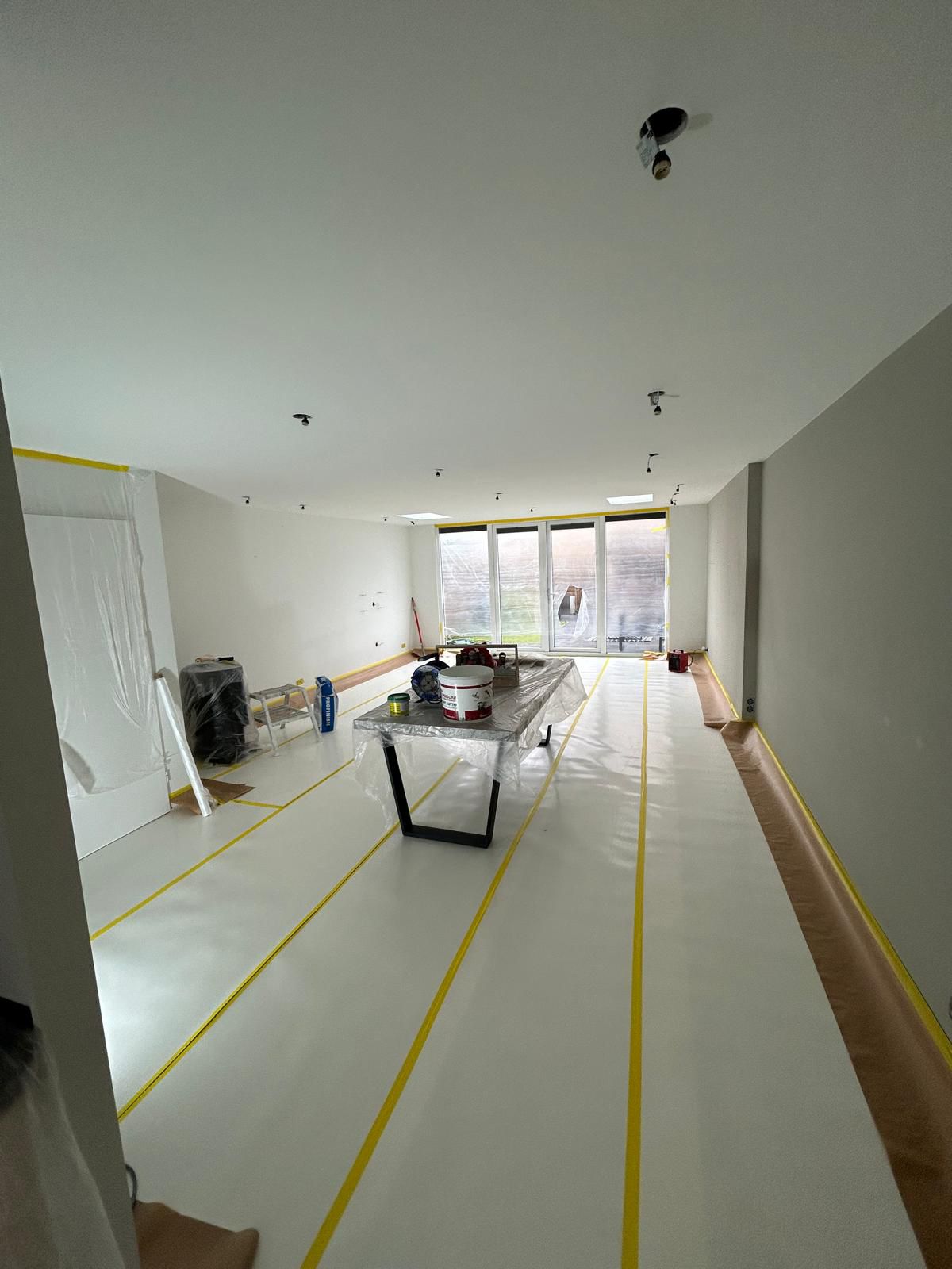 Lange woonkamer met gespoten muren en plafond, vloer afgedekt met folie